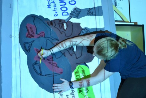 Senior Emily Buterbaugh  traces the lines from a projector as a part of making one of the billboards for the background. 