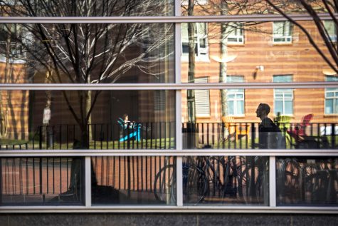 Students are reflected as they walk by the window of West Village on March 17, 2016. Photo by Adam Glanzman/Northeastern University